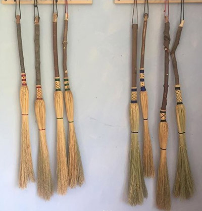 Several rustic brooms hanging from pegs on the wall.